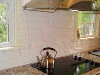 Less can be more in an expansive space. This simple backsplash of solid white glazed tiles provides a clean, maintainable surface behind the reflective cooktop and lets other elements — such as the view through the windows — define the kitchen's atmosphere.