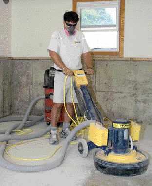To prepare the garage slab for a two-part polyaspartic coating, the author grinds the surface with 50-grit diamond pads. He uses the larger machine.