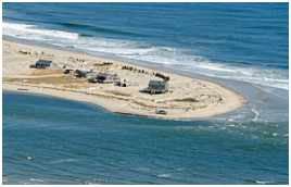 By the spring of 2008, the expanding cut — nibbling its way from right to left in this aerial shot — had already claimed nine cottages and was only days from finishing off the last survivors. Most were moved to relative safety several hundred yards to the north, but the second structure from the right, partially buried in sand by a winter storm, was deemed too far gone to save.