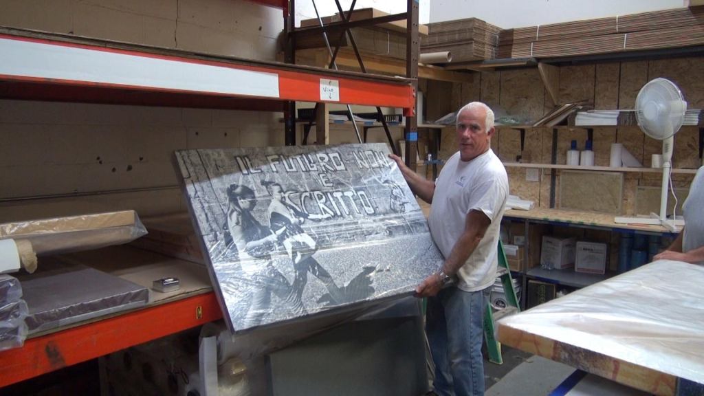 Joseph Drago of New England Soundproofing holds a finished "REVRB" noise-absorbing panel with a screen-printed art surface at his company's Waltham, Massachusetts, shop.