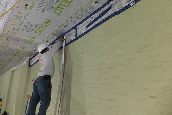 A worker staples ProClima Intello "smart" vapor control membrane to the underside of the building's roof framing. After the membrane is taped to the coated party walls, the air-tight envelope will be continuous—hopefully enabling the building to meet the Passive House specification (see slideshow, "Old School Meets High Tech: Air-Sealing a Brick Row House").