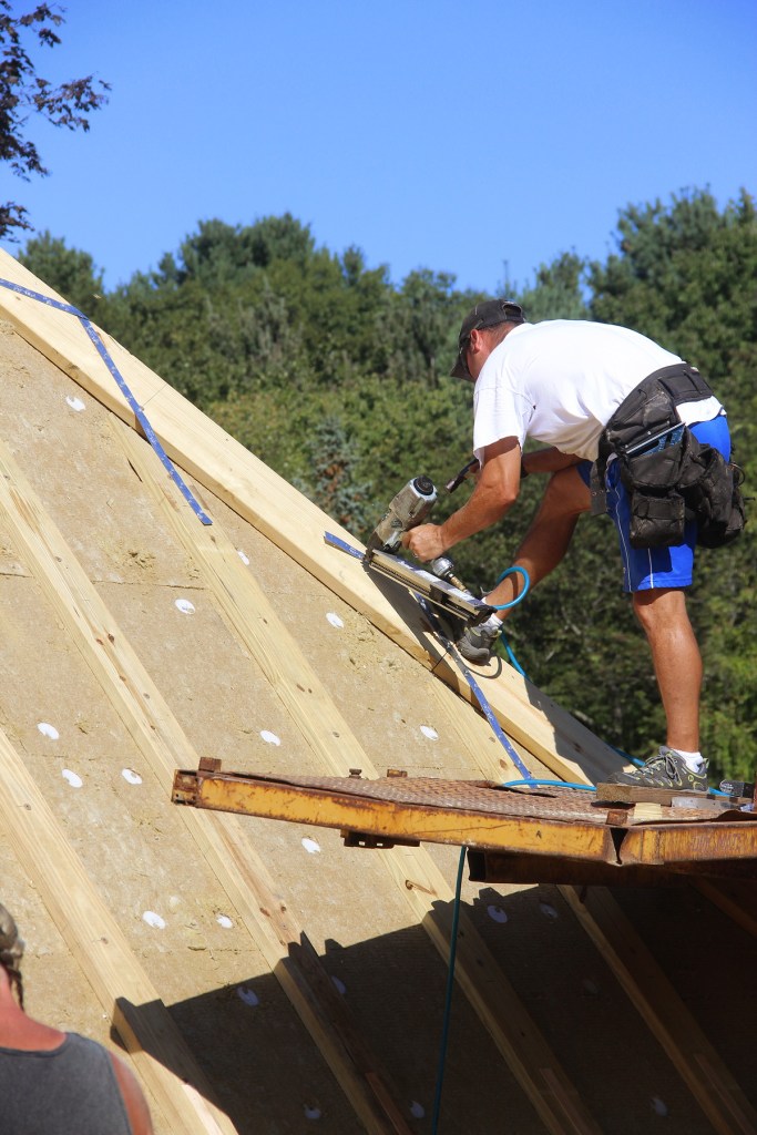 A framer nails reinforcing steel straps to 2x4 furring at the hip, applied over six inches of Roxul rockwool insulation.
