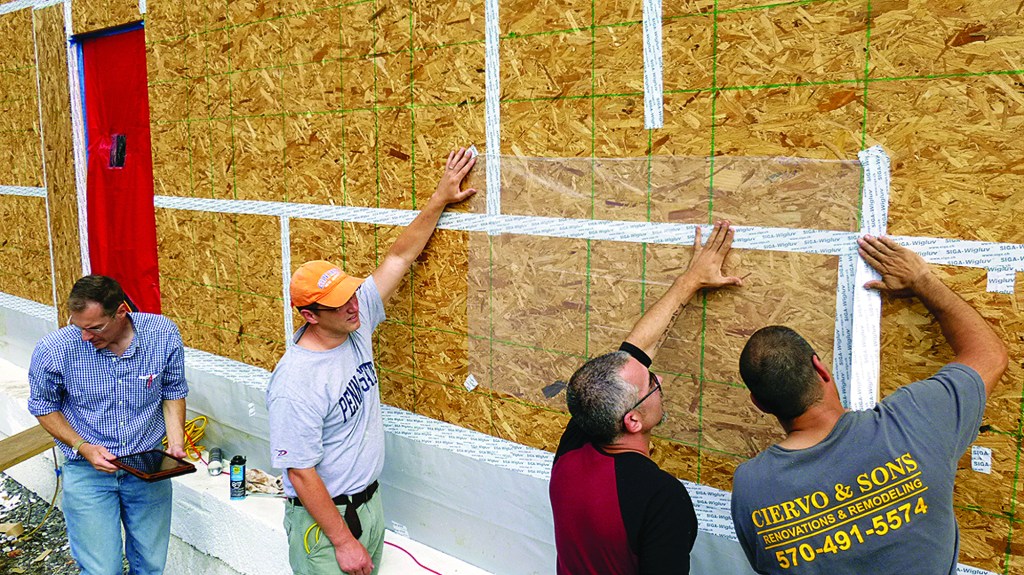 Architect Richard Pedranti, HERS rater Pete Vargo, consultant Bryan Kehm, and builder Rob Ciervo tape plastic over the OSB sheathing during a blower-door test.