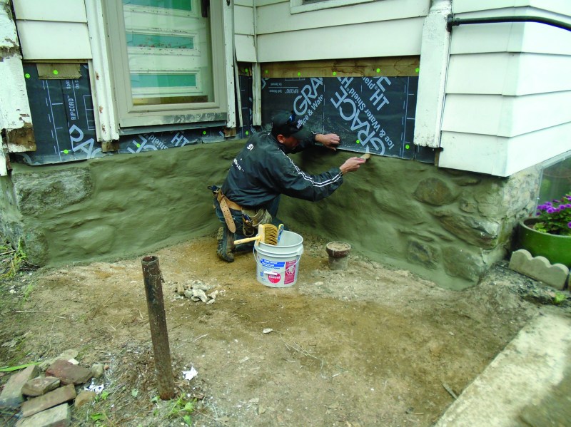 After removing the old deck and peeling back the siding, the author applied membrane on the walls and parged the stone foundation with bonding mortar.
