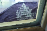 Tempered-glass etching. This etching (shown several times its actual size) on the corner of a glass panel indicates that the glass is tempered. Tempered glass is stronger than conventional plate glass and is used in situations where stronger glass is required, such as for windows at the bottom of a staircase or in a bathroom where a wet floor can be a walking hazard.