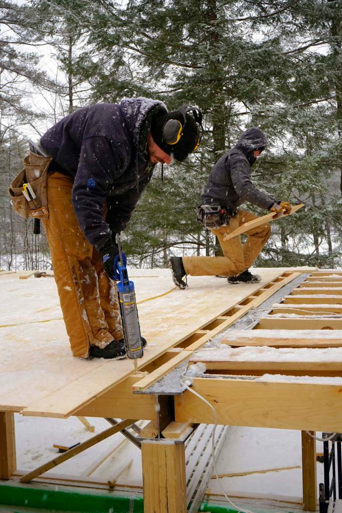 Carpenters Alex Strugatskiy (left) and Ryan Bielenda apply tongue-and-groove pine ceiling boards to sawn timbers as they deck over a lower-level living space for a pond-side home in the Maine woods.