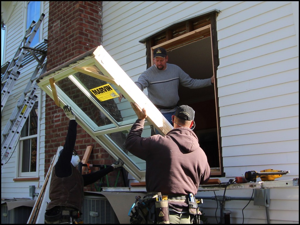 The homeowners wanted to replace their single-pane, two-over-two windows with "true" wood windows. Here, carpenters James Curtis (center), Ed Brady (right), and Isaias Santos (left) lift a full-frame Marvin Ultimate double-hung window in place.