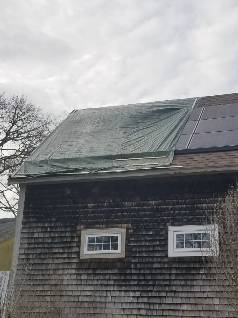 Four days after the fire, a contractor secured a tarp over the damaged roof and panels as storm clouds gathered overhead.