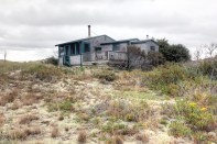 A view of the dune shack showing the main volume of the house stepping down to the bedroom and toilet room. Exterior deck is accessed from the screen porch.