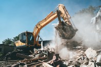 Destruction of old house by excavator. Bucket of excavator breaks concrete structure.