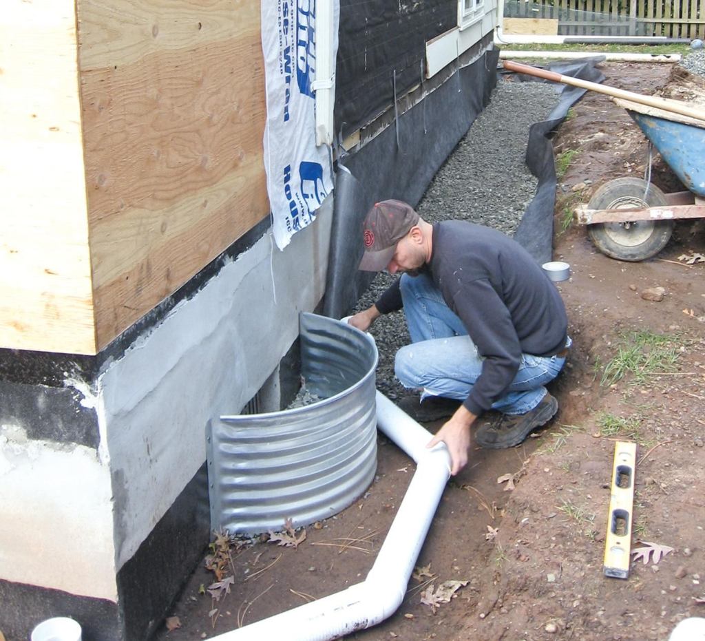 A drainpipe set in coarse stone wrapped with filter fabric — helps manage water around the foundation.