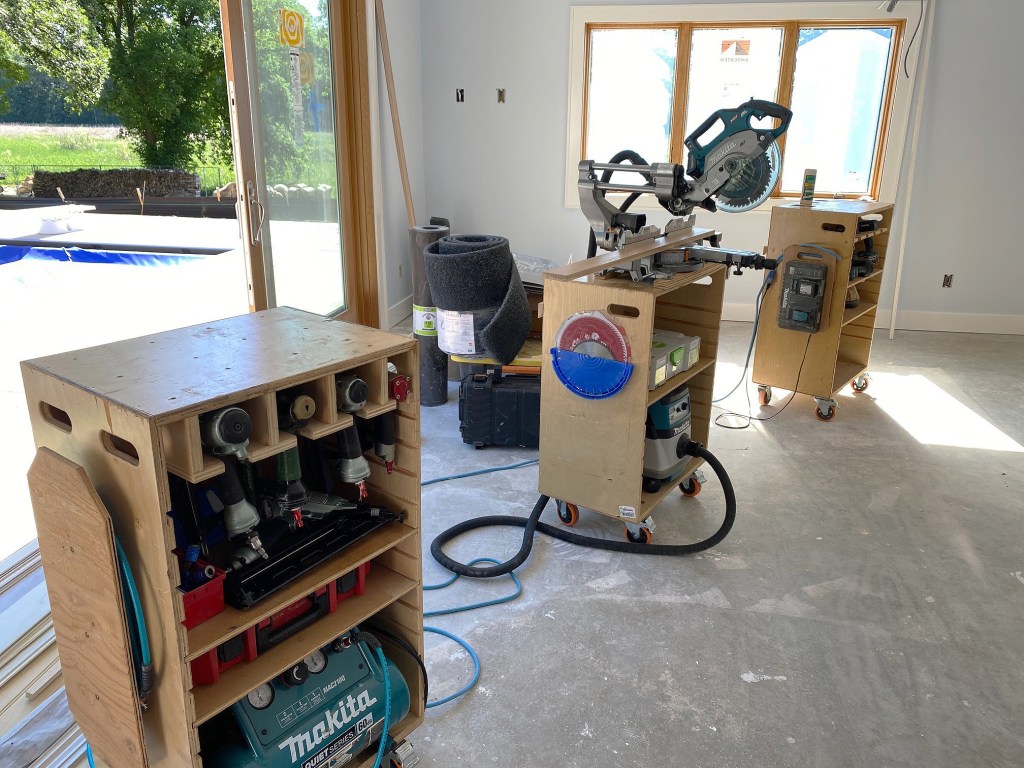 Portable shop. On large trim jobs, the author rolls out tool cases that double as a miter saw stand—a shorter case (center) for the saw and taller cases that function as material supports. The cases organize tools by category: pneumatic tools like air guns and a compressor (at left); cordless tools and chargers (at right).