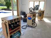Portable shop. On large trim jobs, the author rolls out tool cases that double as a miter saw stand—a shorter case (center) for the saw and taller cases that function as material supports. The cases organize tools by category: pneumatic tools like air guns and a compressor (at left); cordless tools and chargers (at right).