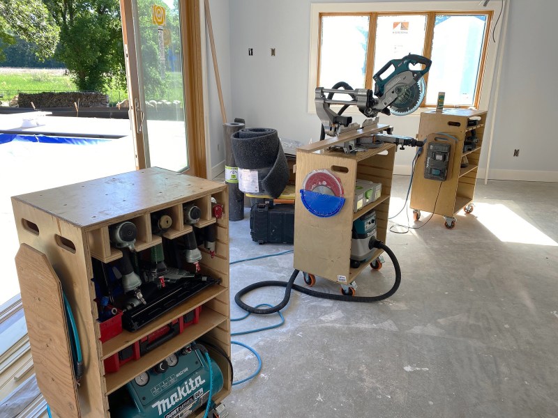 Portable shop. On large trim jobs, the author rolls out tool cases that double as a miter saw stand—a shorter case (center) for the saw and taller cases that function as material supports. The cases organize tools by category: pneumatic tools like air guns and a compressor (at left); cordless tools and chargers (at right).