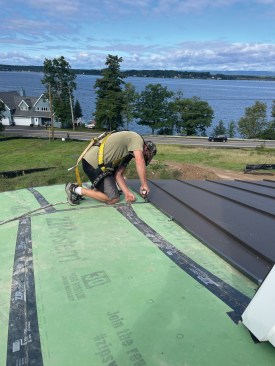 A roofer installs a standing seam aluminum roof on a circular turret.
