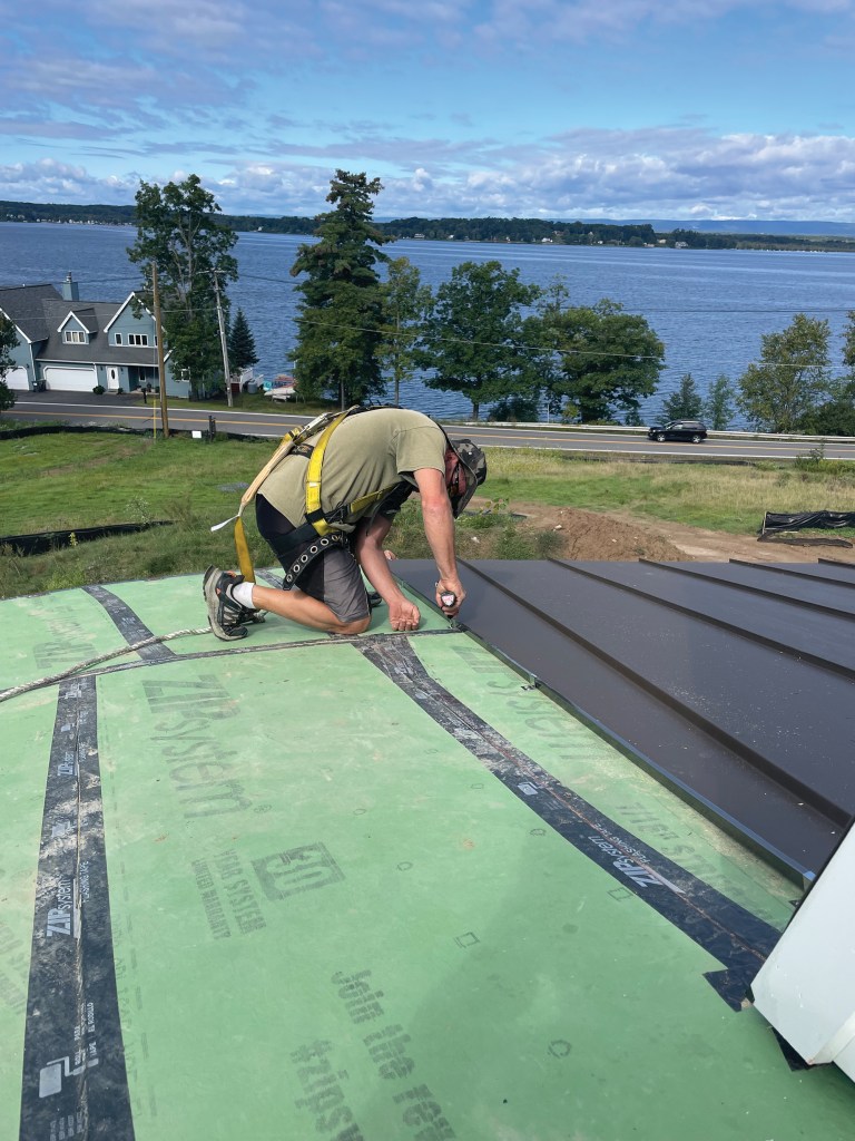 A roofer installs a standing seam aluminum roof on a circular turret.