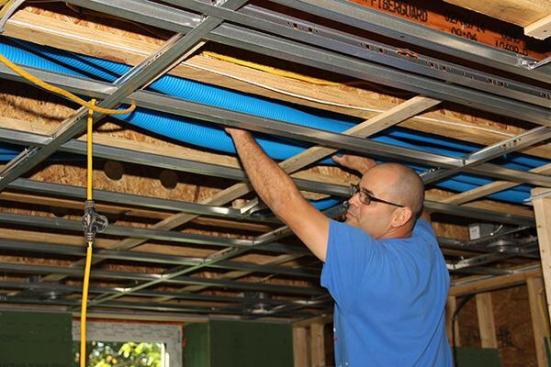 Carpenter Diego Gutierrez runs air supply hoses from Air Pohoda in the ceiling system of the Supply House two-family building. Note the metal suspended-ceiling grid, which is designed for sound-proofing. The metal framework, suspended from the main floor system with wires and used to support the drywall ceiling, will help decouple the downstairs living space from the space upstairs, which is part of the building’s other unit. (The second story of the building is split between two apartments, one of which occupies the entire first floor while the other occupies the entire third floor.)