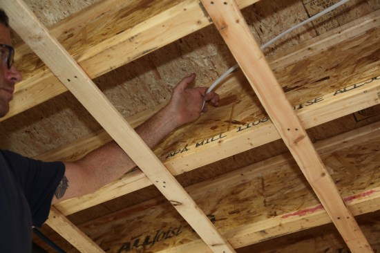 To staple a run of cable to the side of a joist, the author first  hooks the cable with one finger and flattens the cable against the joist with the side of his hand.