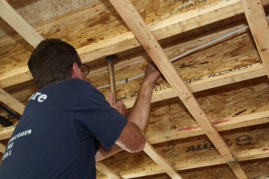 Then he reaches over and pulls the cable
tight while he finishes driving the staple into the joist.