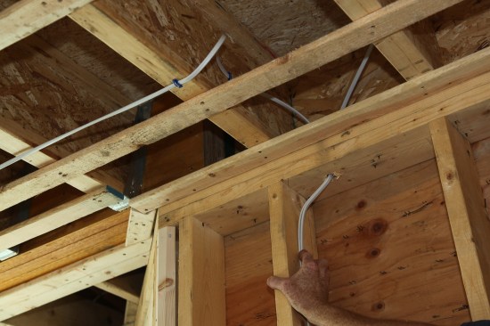 When changing the cable’s direction—from perpendicular to the joists to parallel, or from a horizontal run to a vertical run—the author makes a wide gentle loop to keep the cable flat and relaxed. A staple secures the cable at both sides of the transition. 