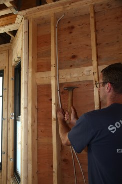 Working down the stud, the author drives staples every few feet, pulling the cables tight as he moves along. 
