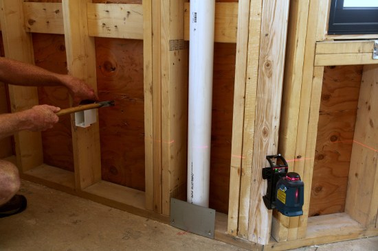 To keep all of the receptacle boxes at the same level, the crew sets up a laser level. They then align the bottom of the box to the laser line before nailing the box in place.