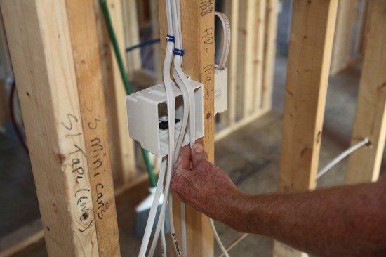This switch box has five cables for two switches. After sorting them out and grouping the cables together, the author gauges the first one for slitting the outer jacket using a finger and thumb.