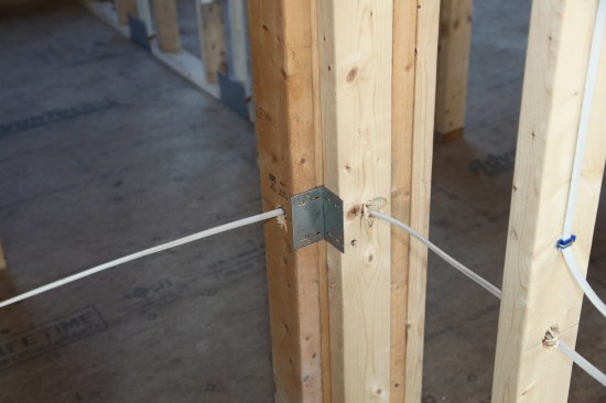 If the cable is within 1 1/4 inches of the stud surface, metal plates are required to prevent damage from errant drywall screws. Here, the angled hole to route
a cable a round a corner is too near the surface, so metal plates protect the cable on both sides of the corner.