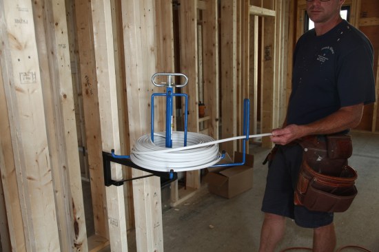 A spooler mounted on a wall stud keeps the cable straight and flat as it comes off the roll. 