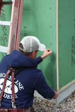 After marking 1 inch at the top and bottom of the wall, a crew member snaps a chalk line to guide placement of the flashing tape at the outside corner. 