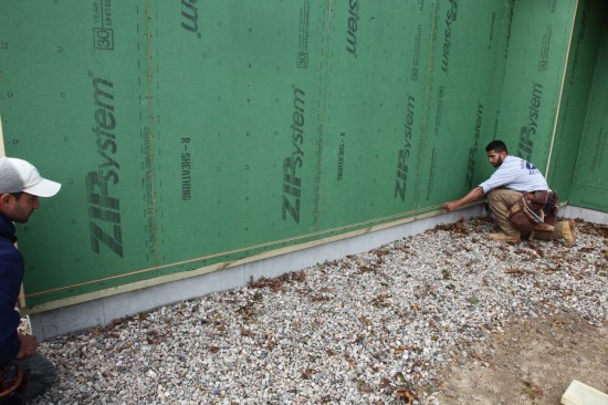 On this project the crew installed a 2x2 treated-wood ledger to close off the exposed foam of the R-Sheathing. The ledger was sealed to the mudsill on the inside, but flashing tape was used on the exterior to ensure a tight seal. The joint along the  bottom had to be taped first. Here the crew snaps a chalk line to guide the tape placement.