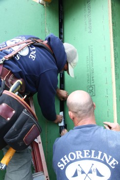 A second length of flashing tape is cut to overlap the lower length by 3 to 4 inches. Installed in a similar fashion, the crewmembers hold one side away from the wall while adhering the first side. 