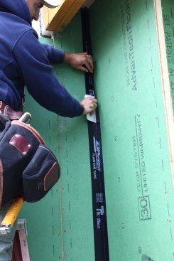 The crew member slowly and deliberately adheres the adjacent side of the corner taking care not to let the tape adhere to sheathing prematurely. When both sides of the tape are positioned properly, a final pass with the roller will make the adhesion permanent.