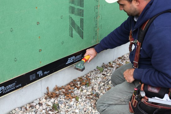 Crew tacks the flashing tape to the treated wood ledger. Treated wood is notorious for not allowing good adhesion without help from some mechanical attachment such as staples. 