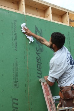 As with all tape applications, installation of tape on vetical joints  begins with wiping down the surface of the sheathing. Note the lines printed on the edge of the panels to guide tape placement.