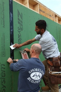 Working from the top of the sheathing, one of the crew unrolls the tape and keeps it on the guidelines while the other uses a plastic spreader for the initial adhesion. 