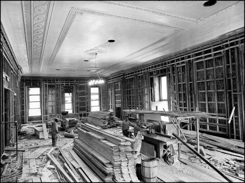 The new ornamental plaster ceiling and wall furring installed in the first-floor East Room. Carpenters work around stacks of lumber destined to become new floorboards.