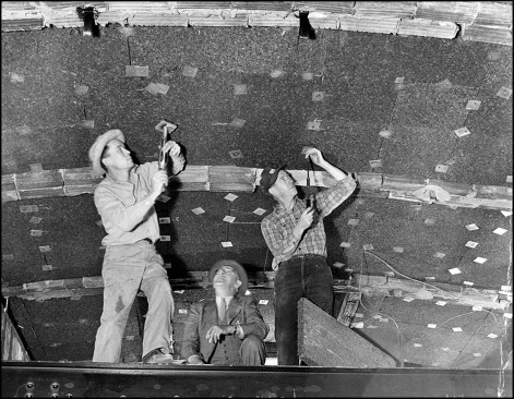 Workmen mechanically fasten cork insulation on ceiling of center hall of third floor.