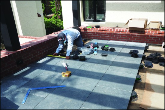A worker installs a ceramic tile paver deck on adjustable pedestals.