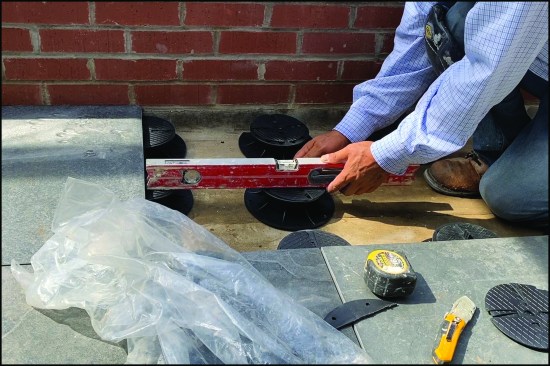 Installation is a simple matter of following the manufacturer’s layout and adjusting the pedestals so that they are level with each other. Here, the 24-inch-by-24-inch-by-3/4-inch-thick ceramic tile pavers are installed (the tile pavers are designed to span over the pedestal bases and typically weigh approximately 50 pounds each).