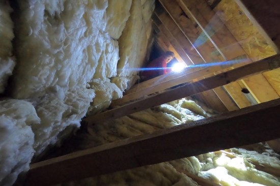 Here, the author investigates the unconditioned space behind the bonus-room knee walls. The bays of the vertical 2x4 web members of the attic trusses (which act as the knee wall) were infilled with 6-inch-thick kraft-faced R-21 batts, while the bays of the 2x10 bottom truss chords were infilled with 9-inch-thick kraft-faced R-30 batts. The ceiling insulation had substantial gaps and voids with some evidence of rodent nesting. The fiberglass batt installation in both the knee wall, ceiling, and connection “hall” area (not shown) were Grade II-level at best with large areas of Grade III work. (For information about insulation assembly grading, see Allison Bailes’ Energy Vanguard blog, “How to Grade the Installation Quality of Insulation” and JLC “Q&A: Installing Faced Batts”.)