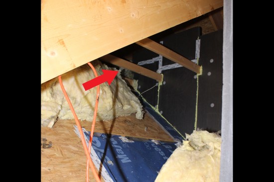 To cover the exposed batts and to make sure the existing baffles would keep venting to the main roof’s ridge vent, Majvest diffusion-open membrane (blue) was taped with Wigluv high-performance tape on the back of the existing baffles; the Majvest was then taped to the sheathing to create a continuous air-seal. Also, the short section of exposed flue pipe was covered with coilstock and Rockwool (red arrow), while 2-inch XPS insulation (dark gray) was mechanically fastened to the connecting hall’s 2x6 framed wall and foamed along the edges and seams.