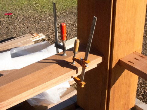 At the red cedar-clad columns, we fit the sub-rails, set to laser level, and fastened them using a Kreg pocket jig and stainless steel screws. The special-order railing cap, cut from 8/4 x 8-inch mahogany, had an 8-degree dual pitch to shed water, with a ¼-inch-deep plough in its underside to accommodate a 2x6 sub-rail.