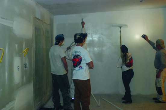 Scott Burt of Prep-to-Finish watches over a group of students as they try the spray-and-roll-over technique of wall finishing.
