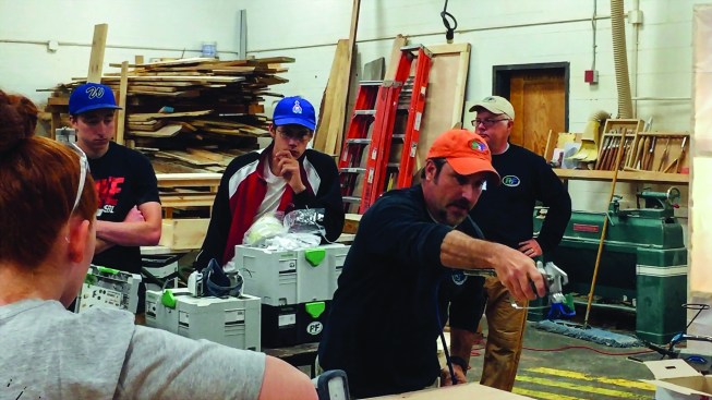Todd Pudvar demonstrates how to spray a finish onto a piece of furniture for students in a vocational school program.