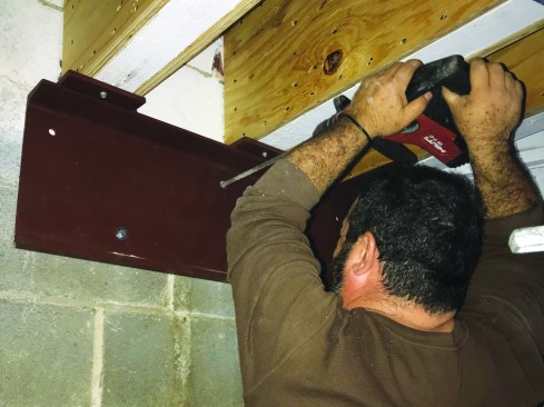 With the beam lag-bolted to the trusses, the crew drilled holes for the anchors.