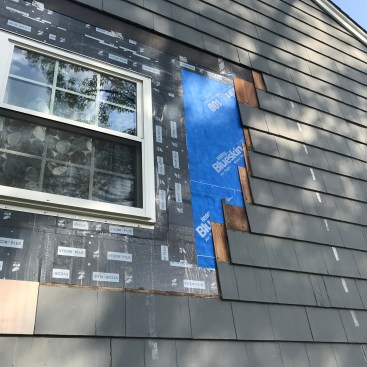 The author next applied adhesive-backed WRB that lapped over the stepped-back shingles, running from the old WRB over to the flashing tape along the sides of the window.