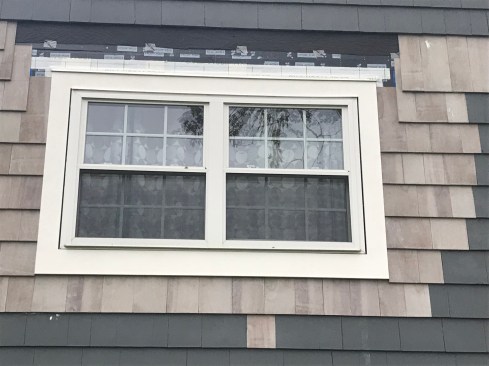New shingles on both sides of the window blend in with the old as the author prepares to wrap shingles over the top of the window. 