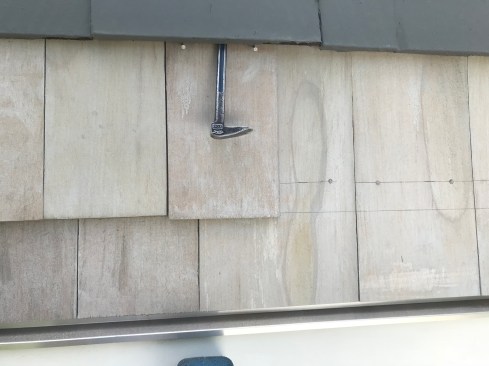 To install the last course of shingles, the author cuts just enough off the tops to keep them from hitting the nails in the course above. After tapping the shingle up to just below the finished level, he angles two shingle nails just below the course above. After driving the nails home, he taps the shingle up to the line, hiding the heads of the nails behind the course above. 