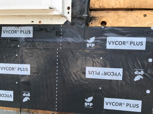 The author began by running wide self-adhering flashing tape up to the bottom window flange, with the side splines lapped over. He then slid a narrow width of flashing tape up under the flange.